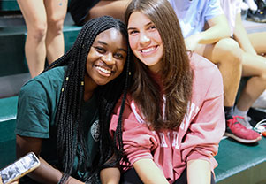 Two girls smiling while sitting in the bleachers. Links to Gifts of Real Estate